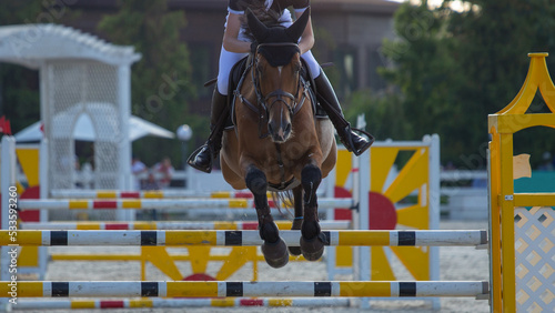 A rider on a horse jumps over an obstacle system in a show jumping competition. Young rider and bay horse, front view.