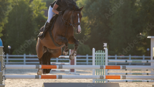 A rider on a bay horse jumps over a high obstacle in a show jumping competition. Equestrian sport.