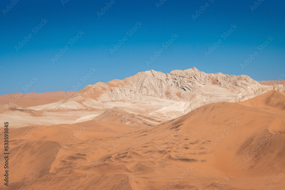 Fototapeta premium mountain in between dunes with blue sky at sossuvlei national park in Namibia, stunning wallpaper