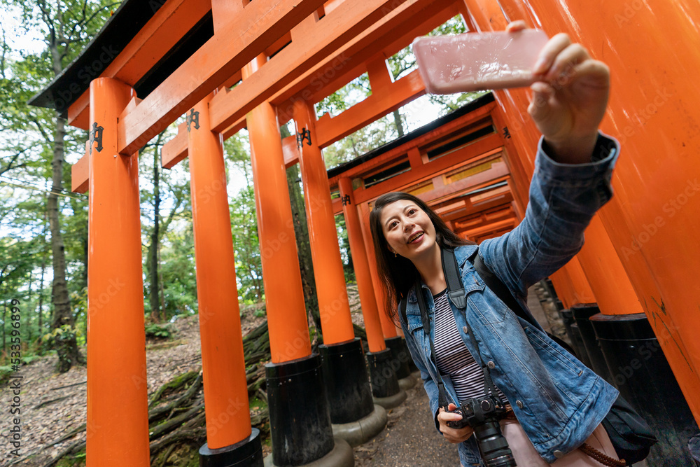 cheerful asian Taiwanese woman visitor having video chat with friends on the phone on Senbon Torii gateway while heading to Fushimi Inari Taisha shrine in Kyoto japan