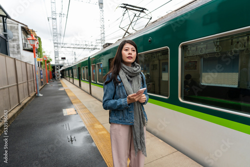 confused asian Japanese woman tourist standing on the platform and looking into distance, not sure which way to go after getting off green train at inari station in Kyoto japan