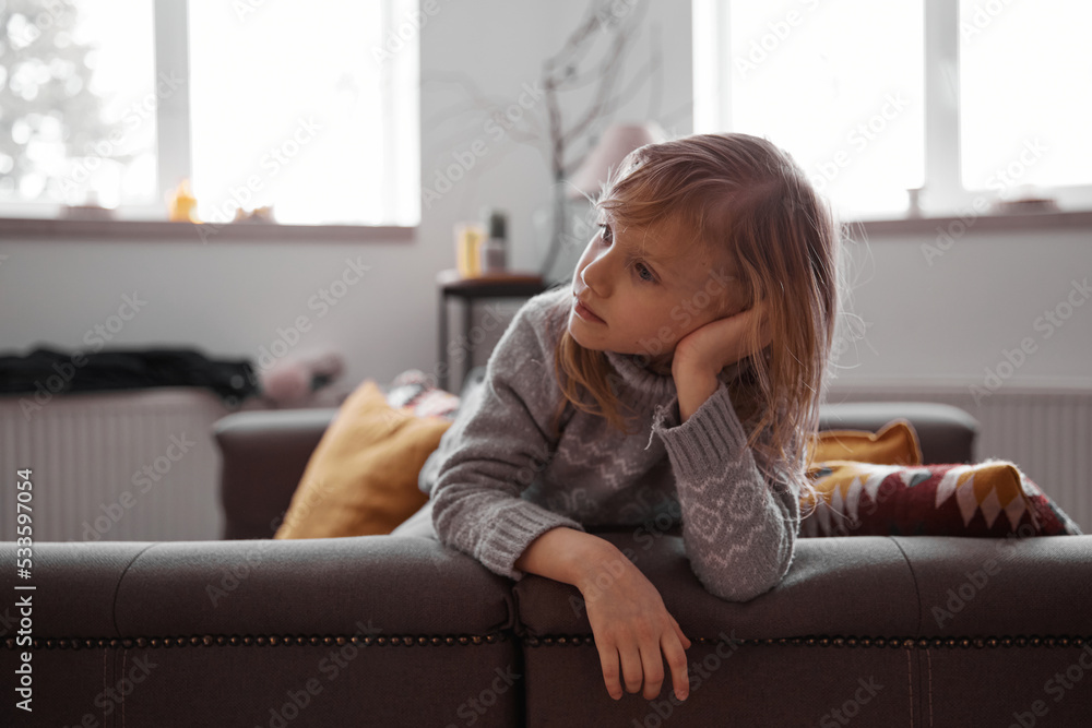 Beautiful little girl sitting on cosiness sofa in the living room at ...