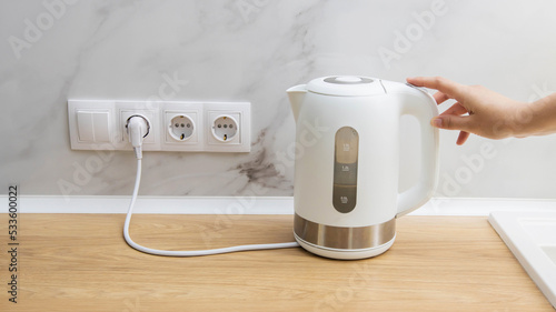 Photos A woman turns on an electric kettle to boil water in the kitchen