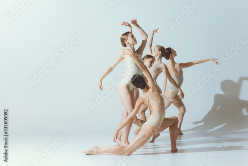 Group of young women, ballerinas dancing, performing isolated over grey studio background. Tenderness, attraction, grace