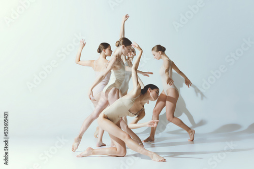 Group of young women, ballerinas dancing, performing isolated over grey studio background. Chaotic movements