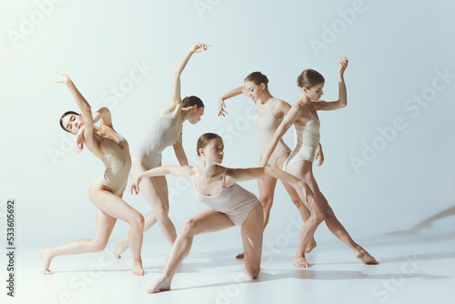 Group of young tender girls dancing, performing isolated over grey studio background. Ballet school, dance education photo
