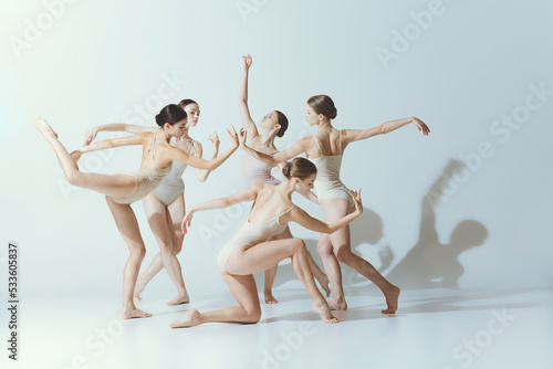 Group of young girls, ballerinas dancing, performing isolated over grey studio background. Adorable dance style