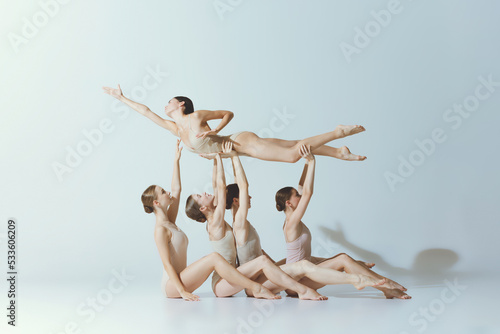 Group of young girls, ballet dancers performing, posing isolated over grey studio background. Giving support