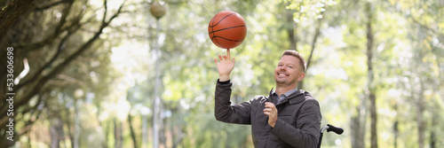 Young smiling man with basketball in wheelchair in park
