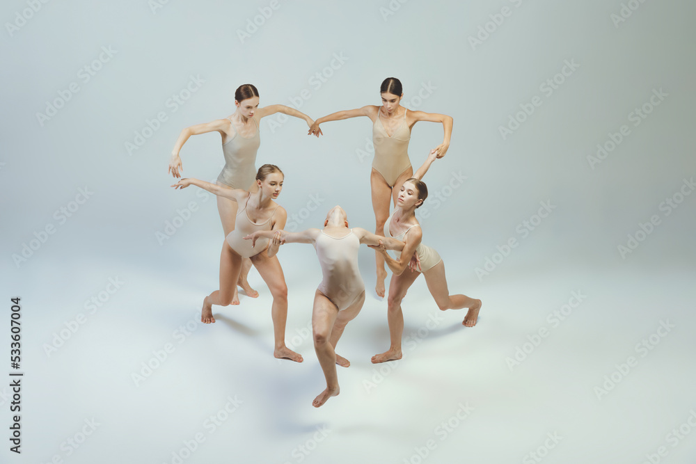 Group of young girls, ballet dancers performing, posing isolated over grey studio background. Heart pose, circle move Group of young girls, ballet dancers performing, posing isolated over grey studio background. Heart pose, circle move