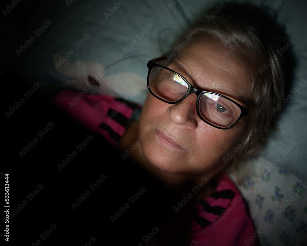 Elderly woman lies on the bed and looks into the smartphone. Elderly woman lies on the bed and looks into the smartphone.