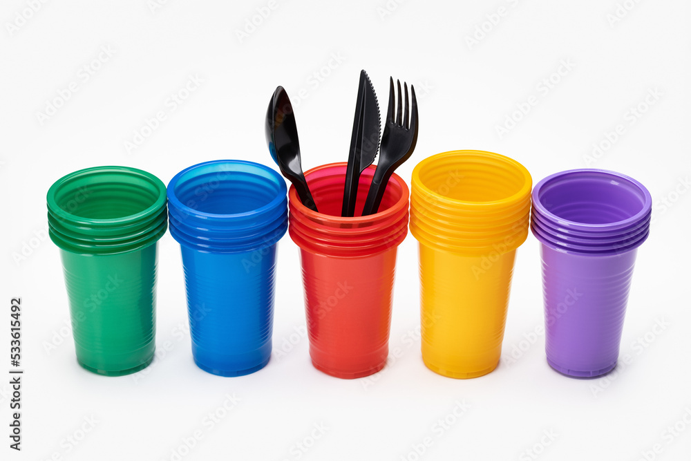 A set, in a row, of multi-colored disposable cups for drinks and cutlery. Isolated, white background.