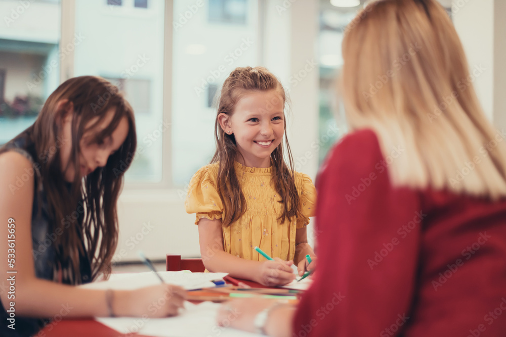 Creative kids during an art class in a daycare center or elementary school classroom drawing with female teacher. Creative kids during an art class in a daycare center or elementary school classroom drawing with female teacher.
