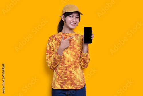young beautiful asian woman demonstrating mobile cell phone isolated on yellow background 
