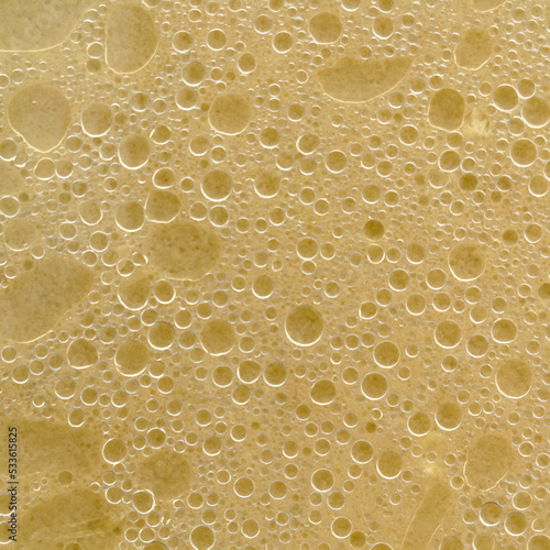 Air bubbles on the surface of the water. Fat rings in an aqueus emulsion. Yellow liquid with bubbles. Square image.