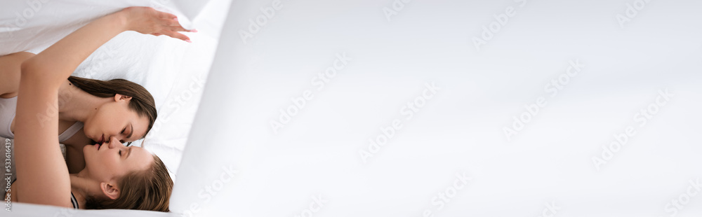 side view of sexy lesbian partners with closed eyes kissing under white blanket, banner. side view of sexy lesbian partners with closed eyes kissing under white blanket, banner.