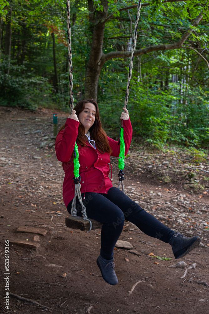 beautiful red-haired woman swinging on a swing on a tree in the middle of the forest