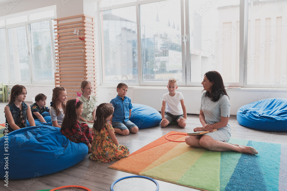 A happy female teacher sitting and playing hand games with a group of little schoolchildren A happy female teacher sitting and playing hand games with a group of little schoolchildren