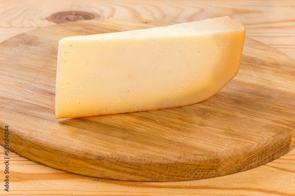 Piece of semi-hard cheese on a round cutting board