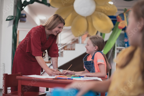 Creative kids during an art class in a daycare center or elementary school classroom drawing with female teacher. 