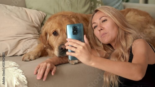 Caucasian blonde woman sitting on carpet with dog Labrador. Happy young student pet owner doing selfie picture, talking and laughing with beautiful Labrador dog at home. 4k footage