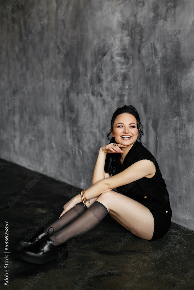A beautiful young brunette woman with makeup in fashionable and trendy clothes poses against a black and gray isolated wall. Sexy model laughs and looks at the camera. Selective focus A beautiful young brunette woman with makeup in fashionable and trendy clothes poses against a black and gray isolated wall. Sexy model laughs and looks at the camera. Selective focus