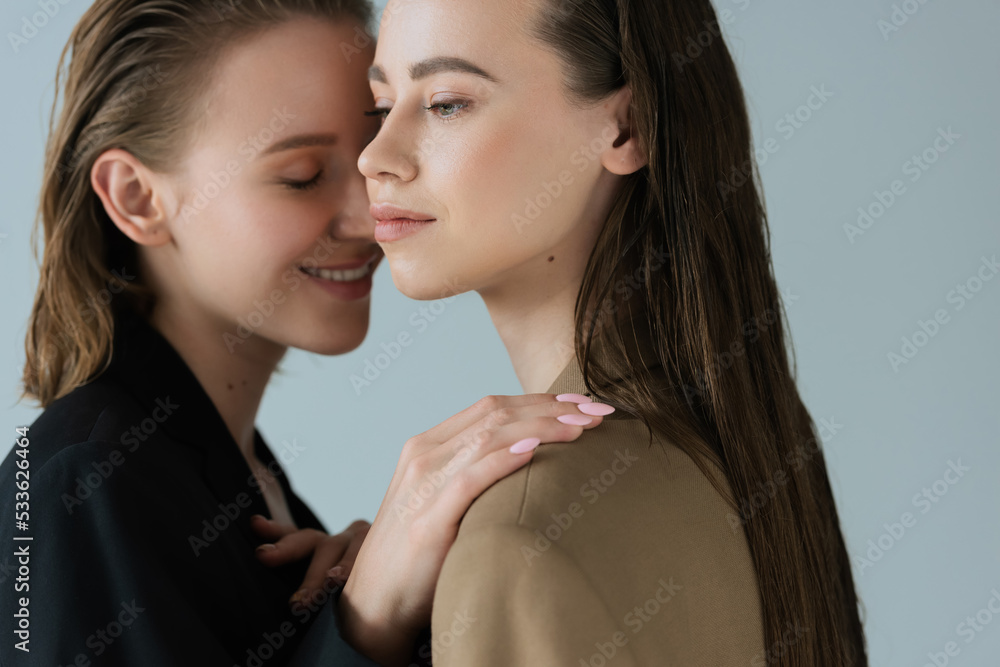 young woman smiling and touching shoulder of lesbian girlfriend isolated on grey. young woman smiling and touching shoulder of lesbian girlfriend isolated on grey.
