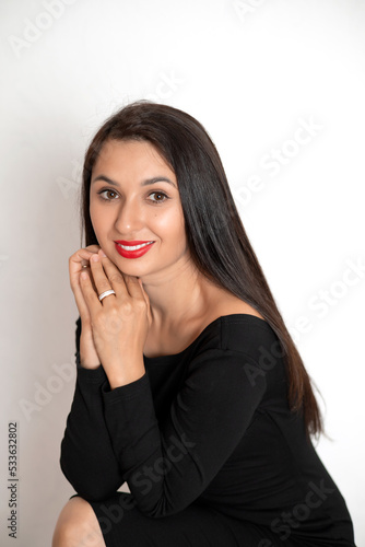 A sensual studio portrait of a beautiful young woman in a black dress with red lipstick on her lips. White background place for text