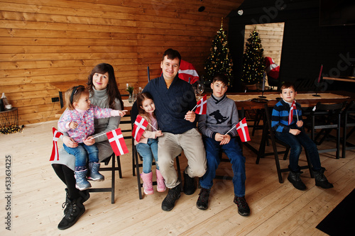 Family with Denmark flags inside wooden house sitting by table. Travel to Scandinavian countries. Happiest danish people's .