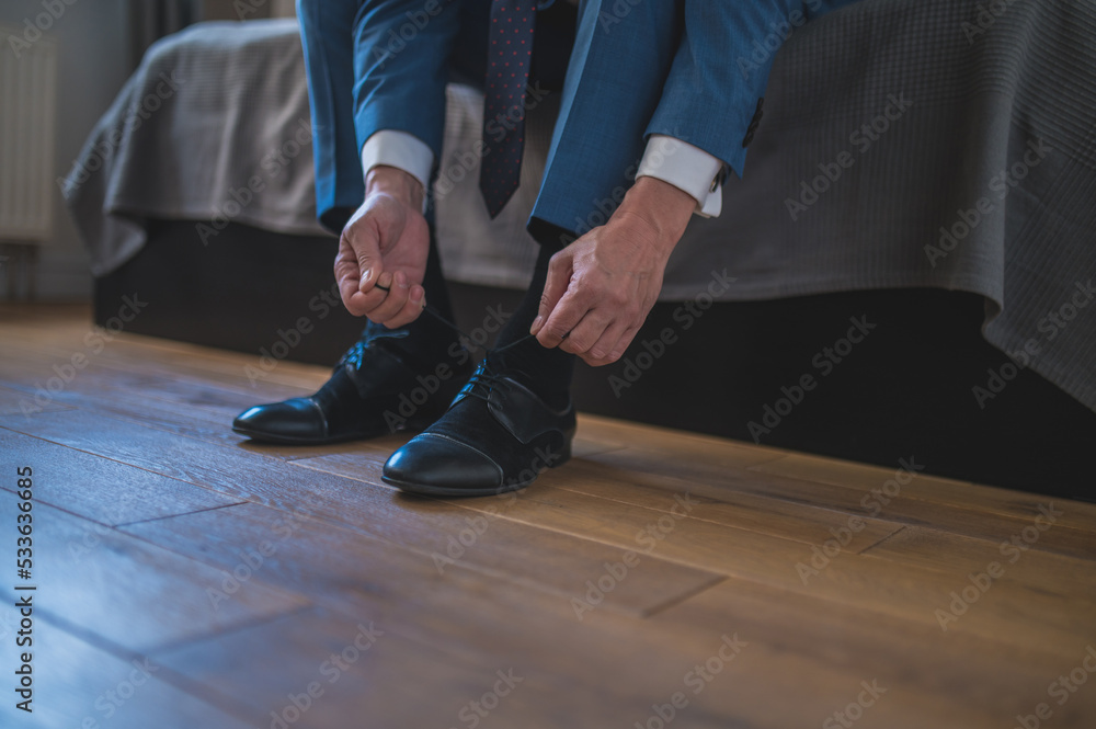 Man in blue suit putting on his shoes wile sitting on the sofa Man in blue suit putting on his shoes wile sitting on the sofa