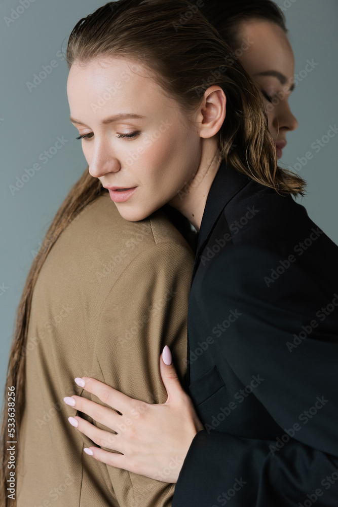 lesbian woman in black blazer hugging young girlfriend isolated on grey. lesbian woman in black blazer hugging young girlfriend isolated on grey.