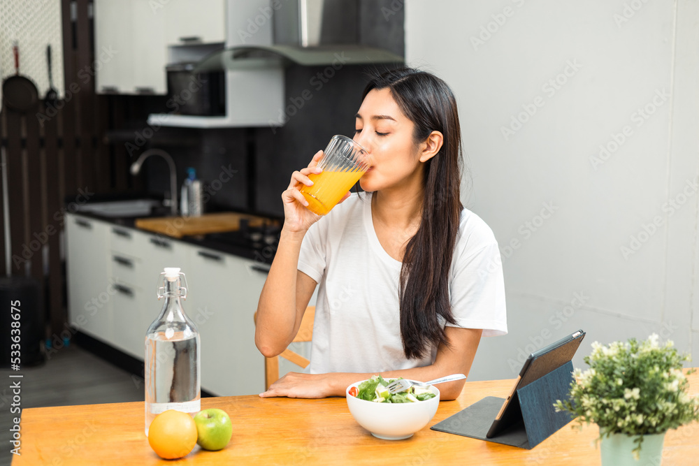 Young female drinking organic orange juice in weight loss diet and wellness on table. Beautiful woman happily drink a healthy fruit juice breakfast in kitchen in the morning. Vitamin c food concept. Young female drinking organic orange juice in weight loss diet and wellness on table. Beautiful woman happily drink a healthy fruit juice breakfast in kitchen in the morning. Vitamin c food concept.