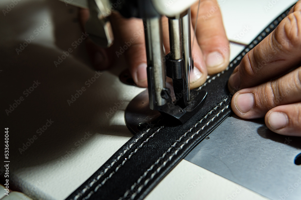 Close up view of Upholsterer's hands sewing leather parts with a sewing machine to fix a seat.