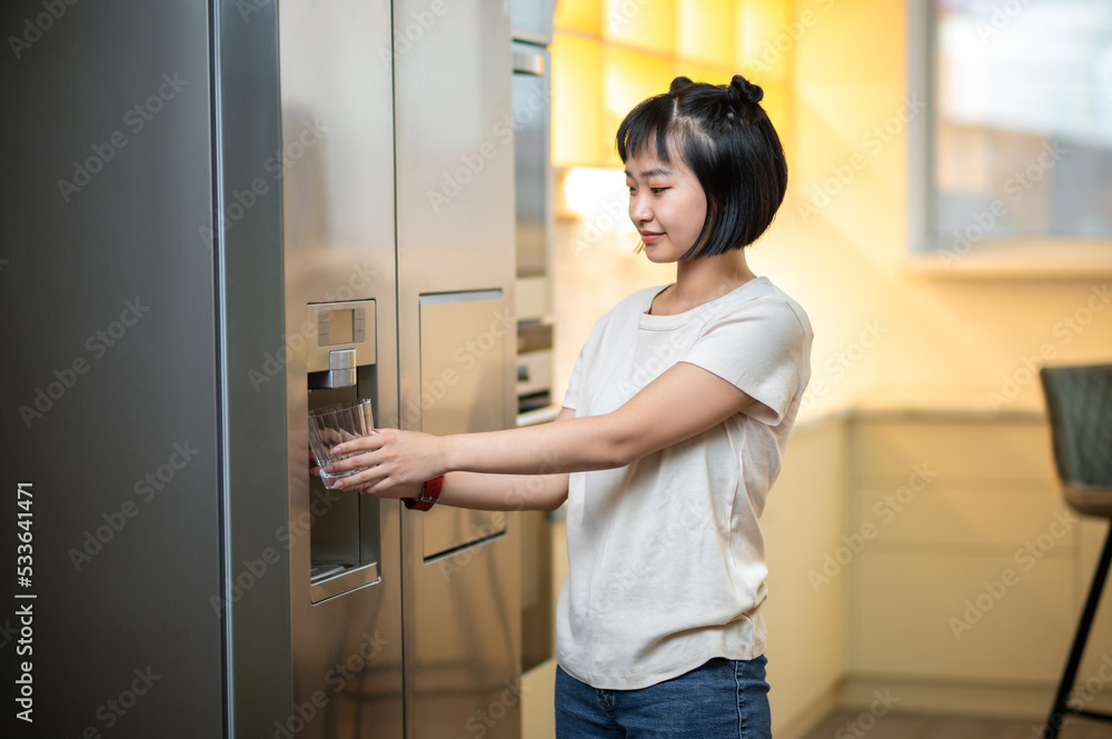 Young female using the refrigerator water dispenser Young female using the refrigerator water dispenser