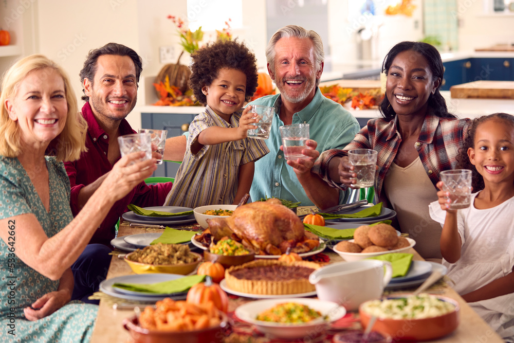 Multi-Generation Family Celebrating Thanksgiving At Home Eating Meal And Doing Cheers With Water