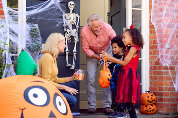 Grandchildren Dressing Up And Visiting Grandparent's House Trick Or Treating On Halloween
