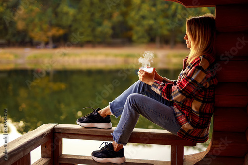 Blonde woman outdoors in check pattern plaid drinking tea near the lake Fototapet