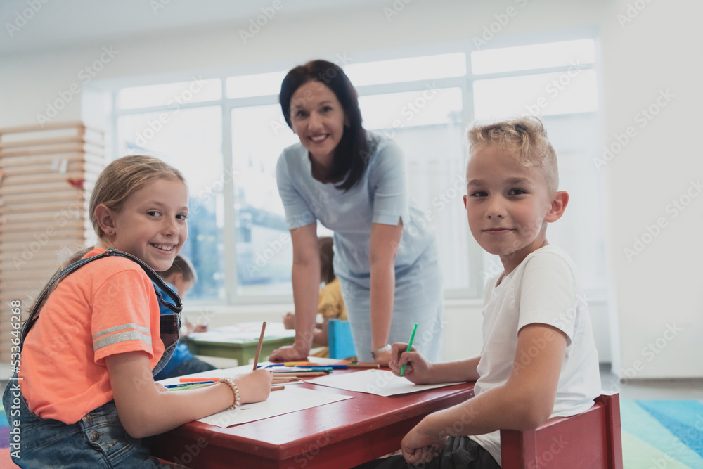 Obraz premium Creative kids during an art class in a daycare center or elementary school classroom drawing with female teacher. 