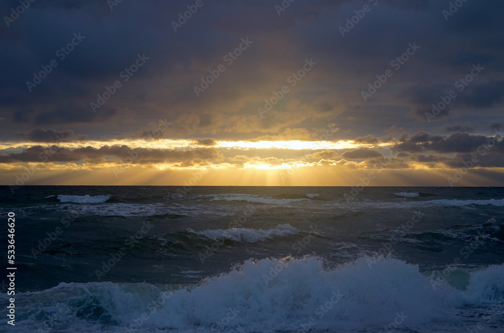 dark clouds of a storm under which sunbeams of the sunset shine on the ocean with waves
