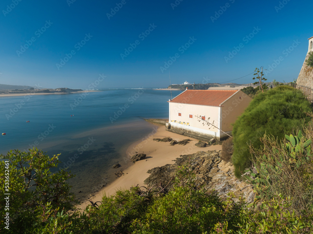 Idyllic view of the mouth of Mira river flowing into the Atlantic Ocean with small beach house and lush green vegetation. Vila Nova de Milfontes, Vicentine Coast Natural Park Portugal