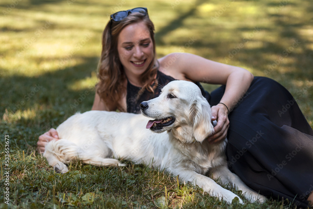 Young woman lying in a grass with a happy golden retriever dog Young woman lying in a grass with a happy golden retriever dog