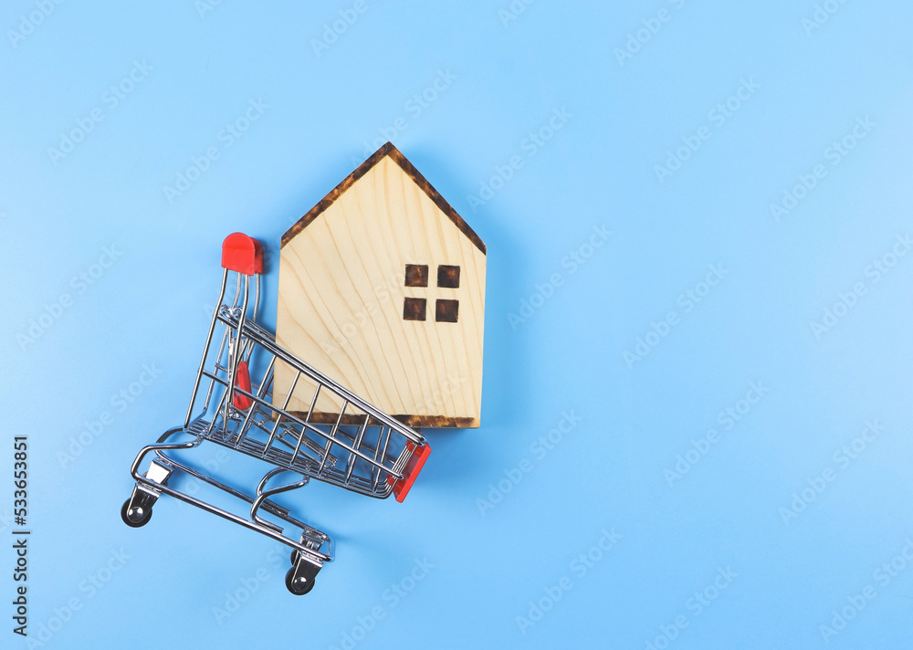 flat layout of wooden house model in shopping trolley on blue  background with copy space, home purchase concept.