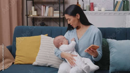 Close up busy mother use phone holding on arms newborn baby crying sitting on sofa in modern apartment. Motherhood. Childhood. Family. Smartphone scrolling. Slow motion