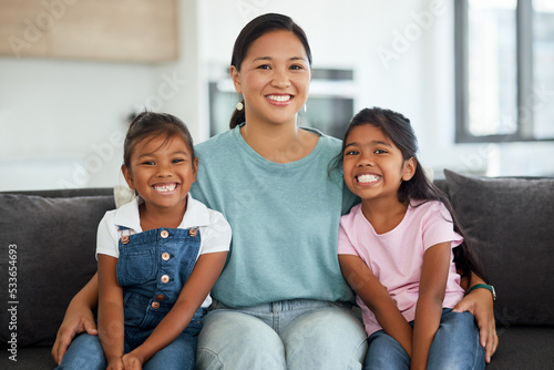 Happy, smile and portrait of a mother and children sitting on a sofa at home in Indonesia. Happiness, love and mom embracing her girl kids while relaxing on a couch together in their living room.