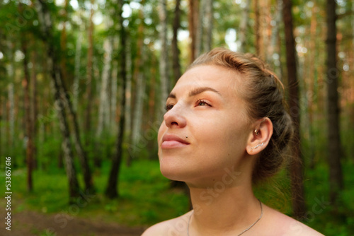 Portrait of a young woman in the forest looking into the distance at the sun. Concept of freedom and unity with nature