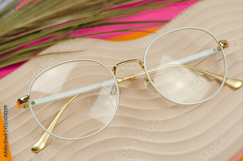 Stylish women's glasses in a white frame on a beige plaster podium