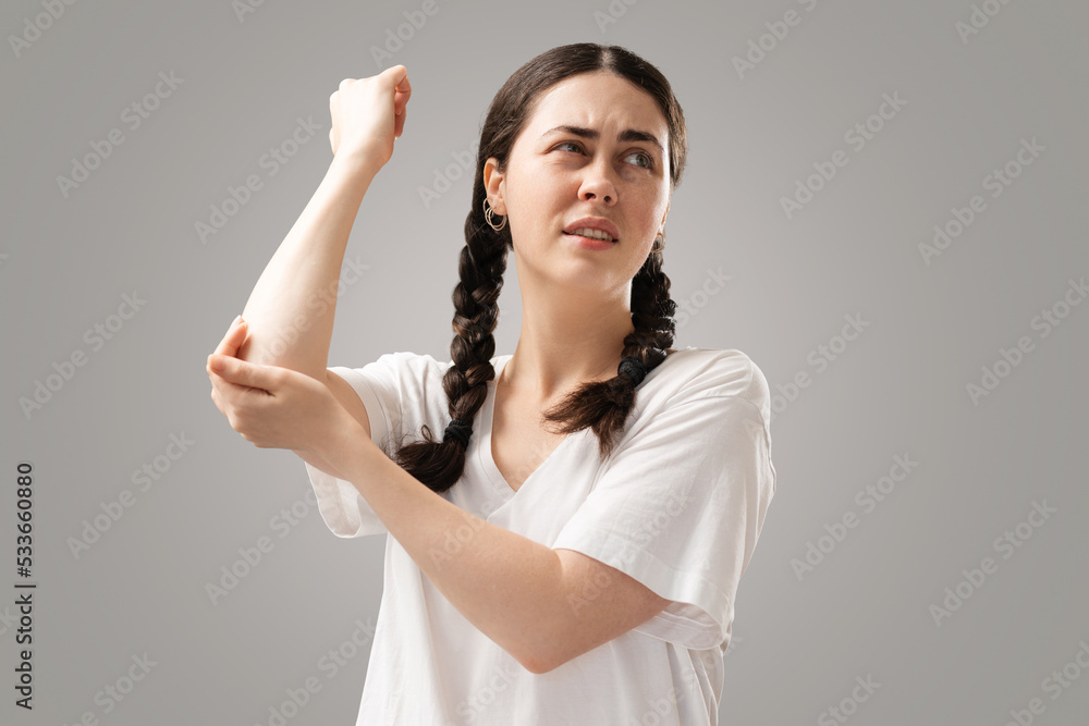 A young woman with dark piggy tails holds her elbow with her hand, feeling pain. Inflammation of the joints. The concept of insurance of health A young woman with dark piggy tails holds her elbow with her hand, feeling pain. Inflammation of the joints. The concept of insurance of health