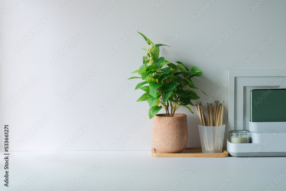 A potted plant, stationery and blank picture frame on white table Home office desk, copy space for your text.