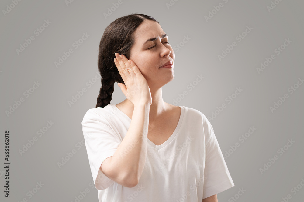 Portrait of young Caucasian woman holds her ear with her palm. The concept of hearing loss, otitis media and tinnitus Portrait of young Caucasian woman holds her ear with her palm. The concept of hearing loss, otitis media and tinnitus
