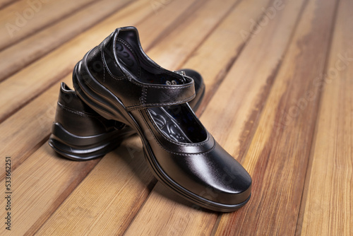 A pair of black female student shoes on wood floor.